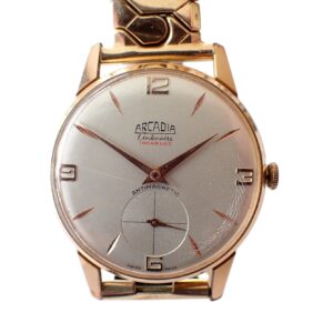 The Arcadia Centenaire watch features a white dial, gold case, gold markers at 12/3/6/9, a small seconds sub-dial, and "antimagnetic" on the face—showcasing vintage style and quality personified.