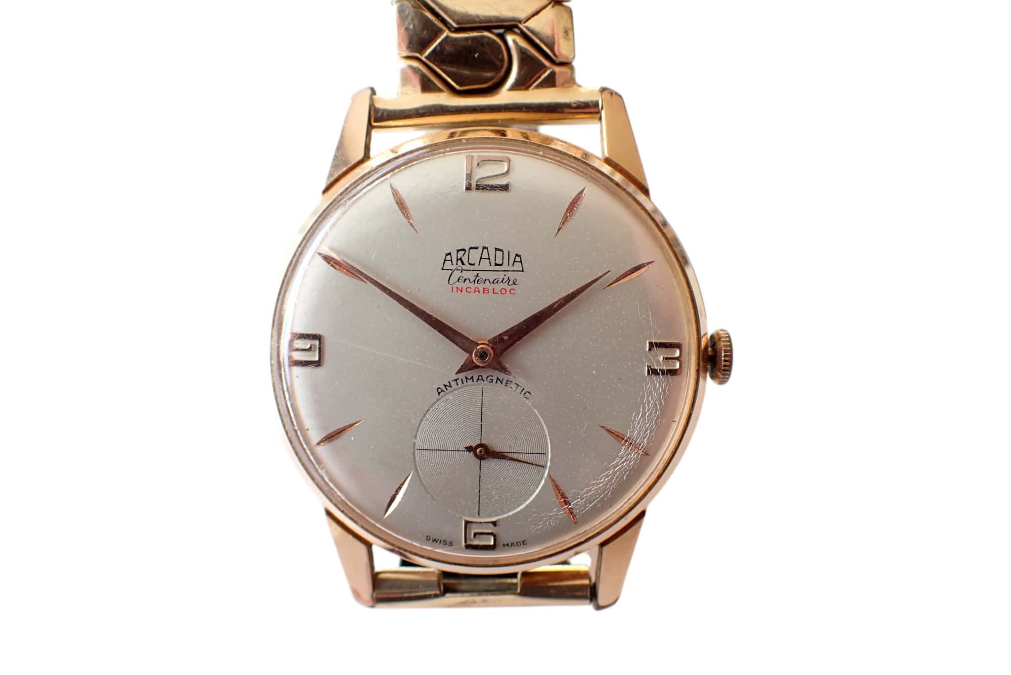 The Arcadia Centenaire watch features a white dial, gold case, gold markers at 12/3/6/9, a small seconds sub-dial, and "antimagnetic" on the face—showcasing vintage style and quality personified.