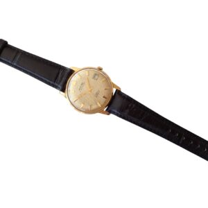 Vintage gold wristwatch with black leather strap on plain white background.