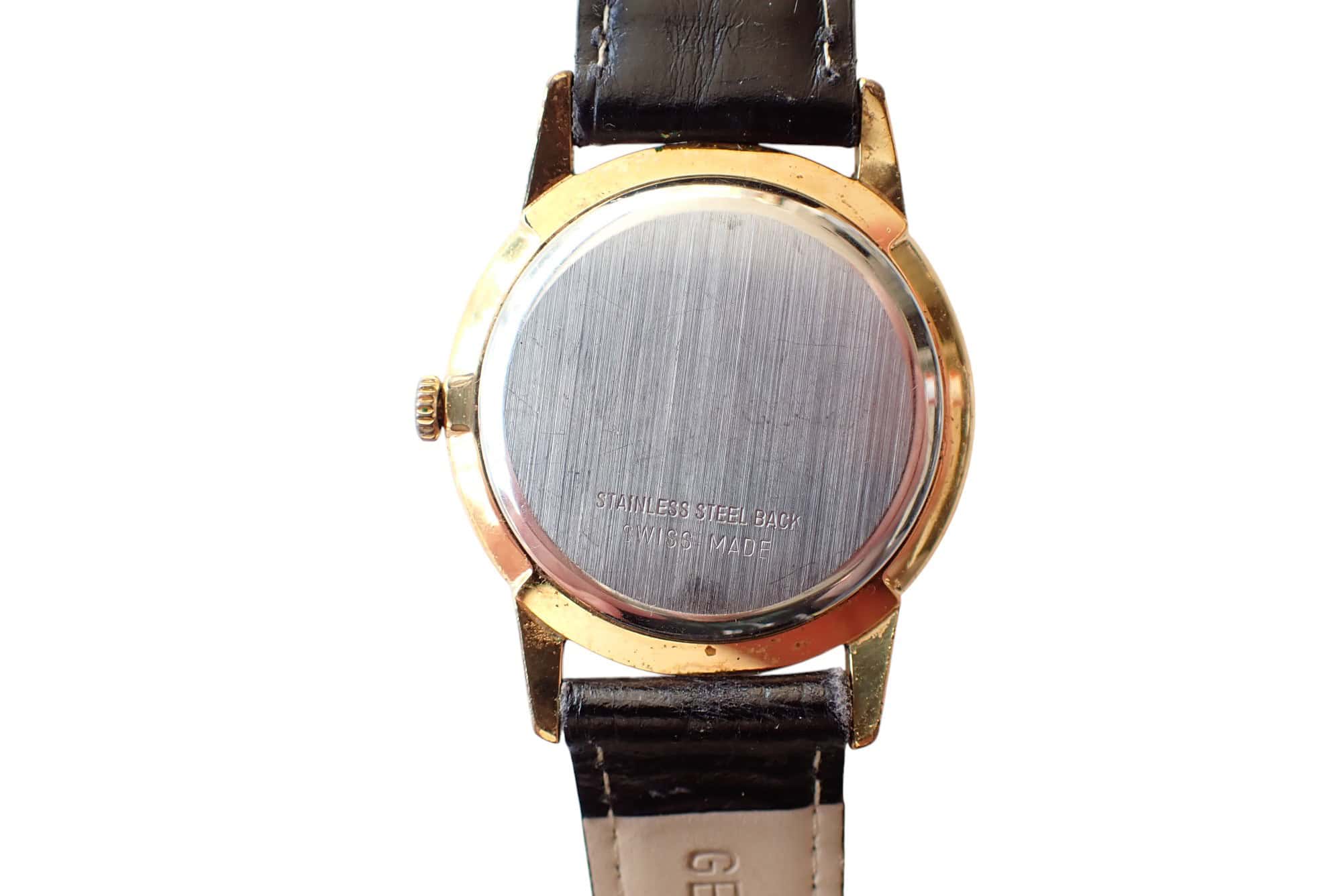 Stainless steel watch back with gold watch case and leather strap, classic vintage design.