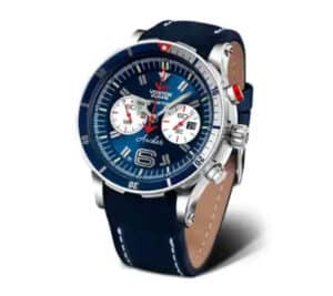 A blue Vostok Anchar wristwatch with a round dial, silver bezel, three sub-dials, and a navy blue leather strap with white stitching. The watch features luminous hands and markers, and bold detailing around the face.