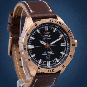 A Vostok Europe Almaz Automatic Line NH35A/320B259 wristwatch features a rose gold case, black dial with white markings, and a brown leather strap, showcased against a blue gradient background.