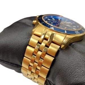 The Swiss Military Hanowa Flagship Chrono Sapphire 06-4183.7/6-51837 gold wristwatch with a blue bezel and gold metal strap is displayed on a black leather cushion against a white background.