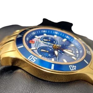 A close-up of the Swiss Military Hanowa Flagship Chrono Sapphire 06-4183.7/6-51837 gold wristwatch with a blue bezel and dial, three sub-dials, and luminous hands, shown on a black gloved hand against a white background.