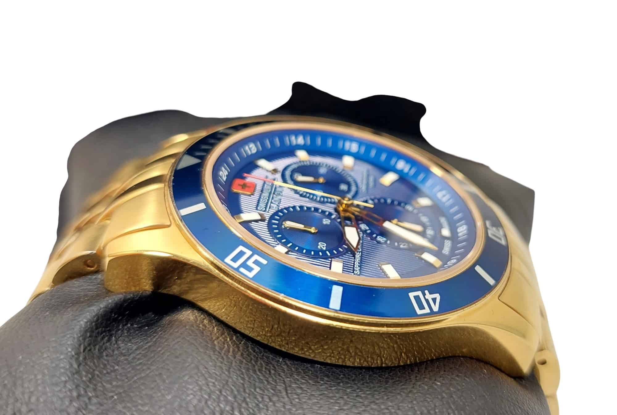 A close-up of the Swiss Military Hanowa Flagship Chrono Sapphire 06-4183.7/6-51837 gold wristwatch with a blue bezel and dial, three sub-dials, and luminous hands, shown on a black gloved hand against a white background.