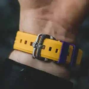 A close-up of a wrist wearing the NUBEO SKYLAB AUTOMATIC LIMITED EDITION Indigo NB-6083-0H, featuring a yellow strap with a silver buckle and purple loops, set against a dark, blurred background.